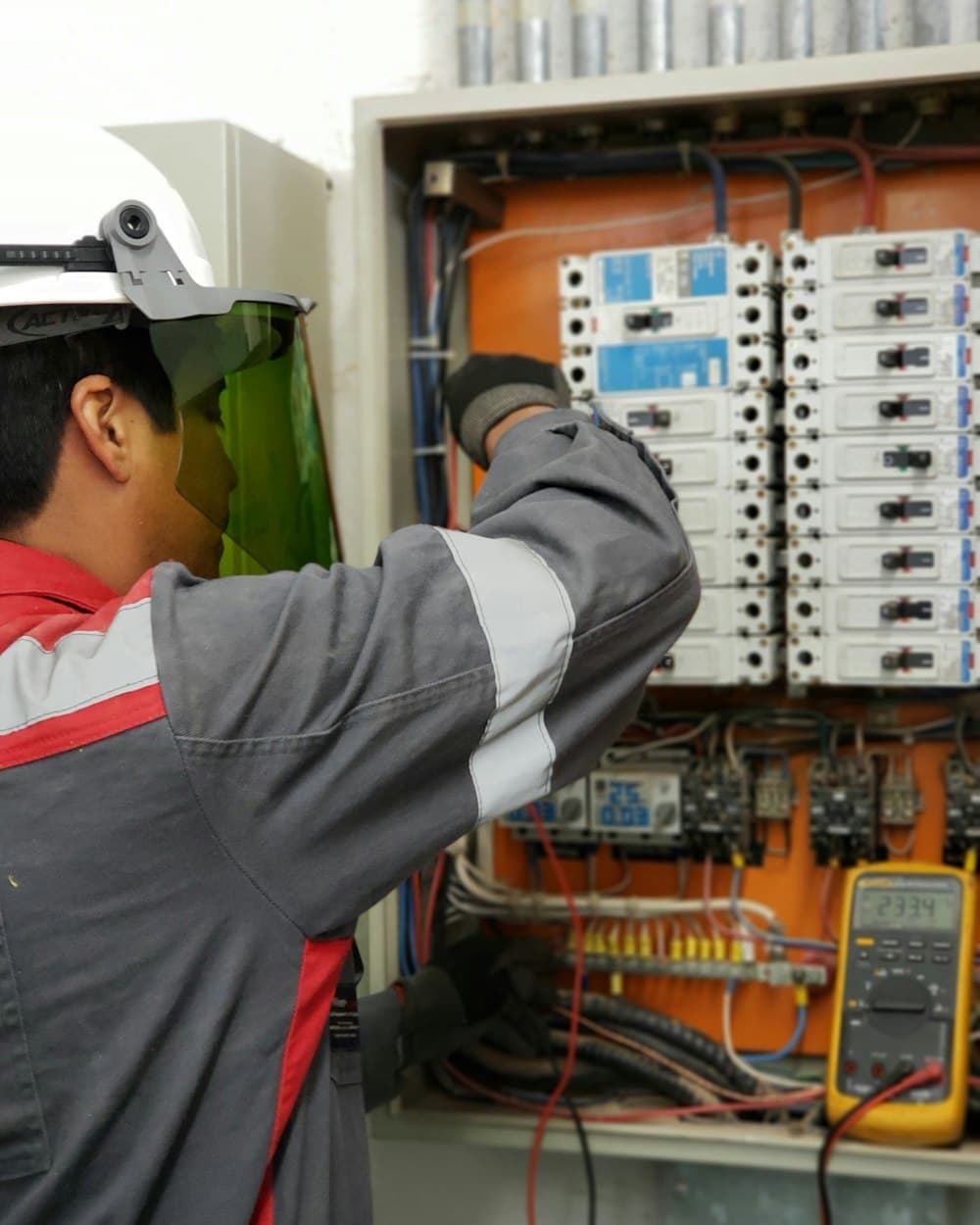 Electrician in a face shield testing an electrical panel